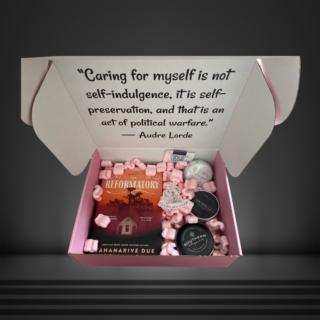 A pink box with an Audre Lorde quote that has a book, sticker, magnetic bookmark, candle, under eye mask, and bath bomb inside.